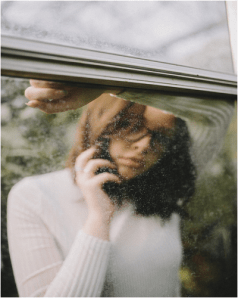 picture of girl on phone behid dirty window